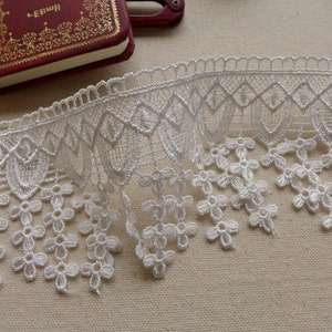 May include: White lace trim with a scalloped edge and a delicate floral pattern. The lace has a fringe of small flowers.
