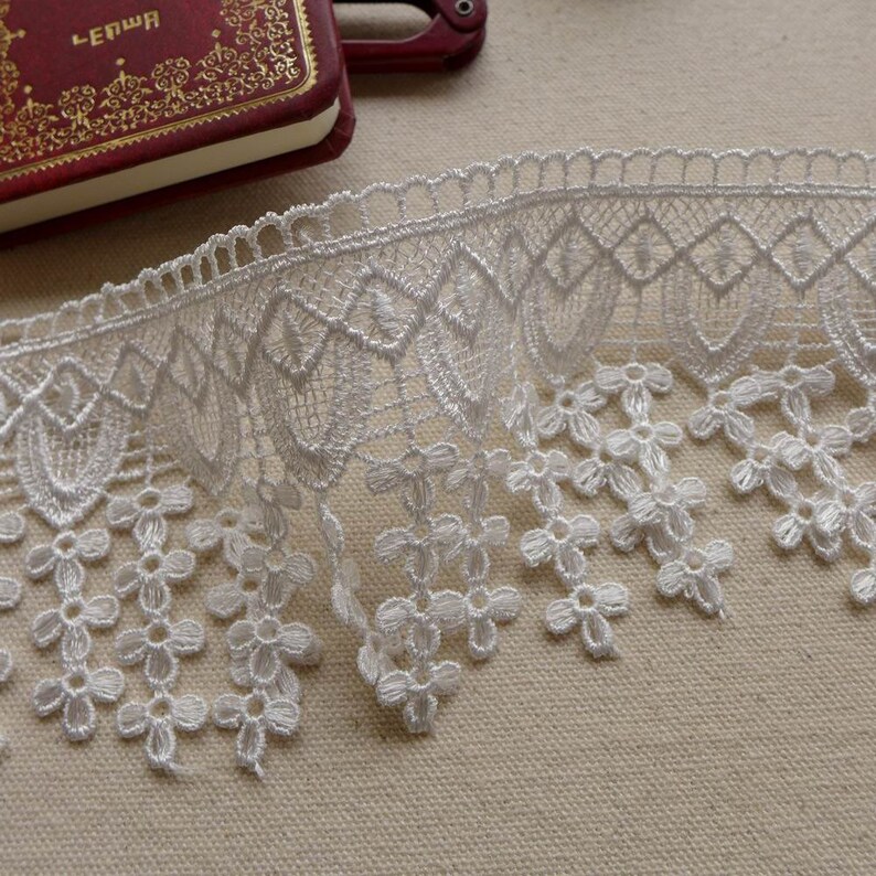May include: White lace trim with a scalloped edge and a delicate floral pattern. The lace has a fringe of small flowers.