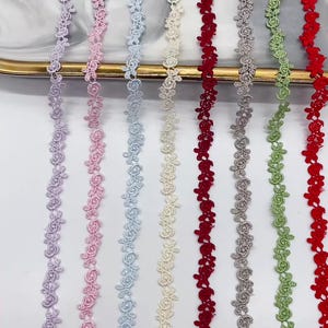Puede incluir: Ocho tiras verticales de encaje floral dispuestas una al lado de la otra. Los colores incluyen lavanda, rosa claro, azul claro, crema, rojo oscuro, gris, verde claro y rojo brillante. Cada tira presenta un patrón repetitivo de rosas.