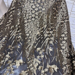 May include: Black sheer fabric with gold floral embroidery. The fabric has a delicate, intricate design.