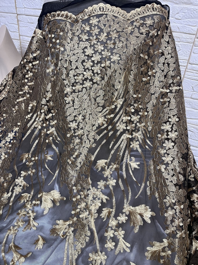 May include: Black sheer fabric with gold floral embroidery. The fabric has a delicate, intricate design.