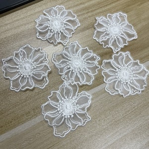 May include: Six white floral appliques featuring sheer organza petals with intricate white embroidery outlining the edges and a detailed stitched center. These decorative flower patches are crafted with a delicate, semi-transparent fabric construction.