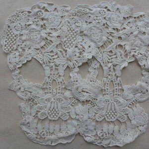 May include: Two white lace skull shapes, made of delicate floral patterns, are joined together at the top. The lace is intricate and detailed, with a delicate, almost translucent quality.
