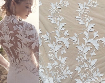 May include: White floral lace fabric with a delicate pattern of leaves and flowers. The lace is sheer and has a soft, flowing texture.