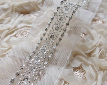 May include: White tulle ribbon with a beaded trim. The trim features a geometric pattern of clear rhinestones and silver beads.