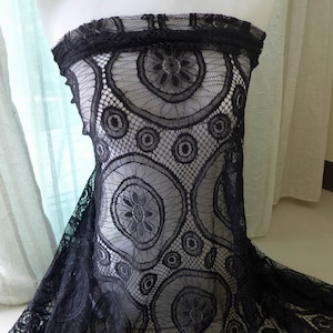 Peut inclure: Un haut bustier en dentelle noire pr&eacute;sentant un motif r&eacute;p&eacute;titif de grands et petits cercles avec des centres floraux complexes. Le tissu l&eacute;ger et transparent est drap&eacute; sur un mannequin, mettant en valeur la texture d&eacute;taill&eacute;e du maillage.