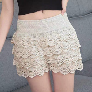 May include: A white lace skirt with multiple layers and a scalloped hem. The skirt is made of delicate crochet fabric and has a fitted waistband.
