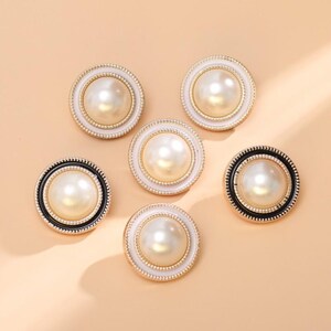 May include: Six circular buttons featuring a central faux pearl surrounded by a gold-toned beaded ring. Three buttons have a white outer border, while the other three buttons feature a contrasting black outer border, all arranged in a cluster.