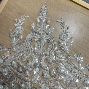Pu&ograve; includere: Primo piano di un tessuto perlato argento e bianco con un motivo floreale. Il tessuto &egrave; fatto di paillettes e perle.