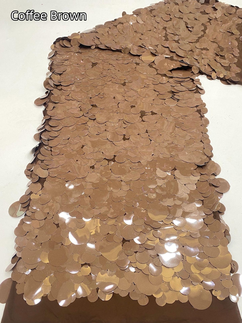 Puede incluir: Una tela de color marr&oacute;n caf&eacute; con una capa densa de lentejuelas circulares superpuestas. El material tiene un acabado met&aacute;lico reflectante y est&aacute; etiquetado con el texto Coffee Brown en la esquina superior izquierda, mostrando una textura uniforme.