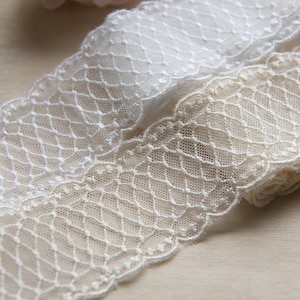May include: Two pieces of white lace trim with a delicate diamond pattern. The lace is soft and sheer, and it would be perfect for adding a touch of elegance to any project.