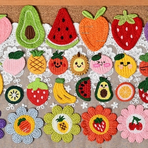 May include: A collection of colourful crochet appliques featuring various fruits, vegetables, and flowers. The assortment includes shapes of avocados, watermelon slices, carrots, strawberries, pineapples, bananas, kiwis, and daisies with fruit centres.