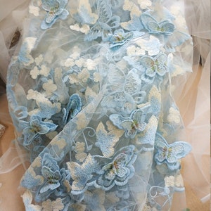 Pu&ograve; includere: Tessuto trasparente azzurro chiaro con farfalle ricamate. Le farfalle sono di diverse dimensioni e hanno un contorno bianco.