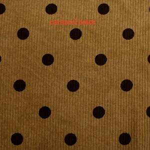 May include: A caramel-colored corduroy fabric featuring a repeating pattern of dark brown polka dots. The textile has a distinct vertical ribbed texture throughout, with the text "caramel color" printed in red across the upper center area.