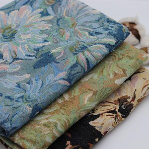 May include: Three folded pieces of woven fabric stacked together. The top layer features a blue and light blue floral pattern. The middle layer displays a green and tan floral design. The bottom layer shows a black, tan, and white floral print.