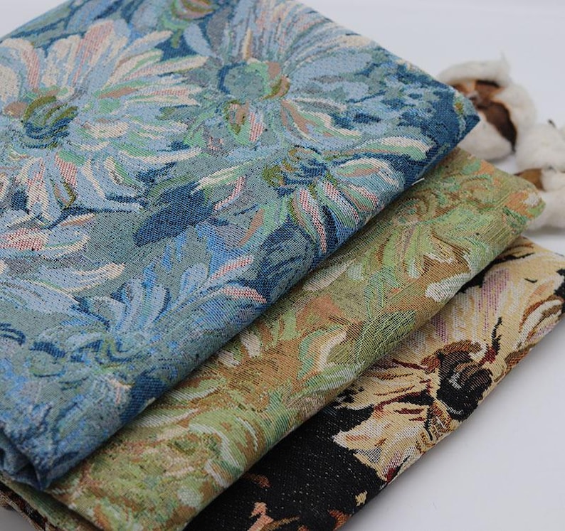 May include: Three folded pieces of woven fabric stacked together. The top layer features a blue and light blue floral pattern. The middle layer displays a green and tan floral design. The bottom layer shows a black, tan, and white floral print.
