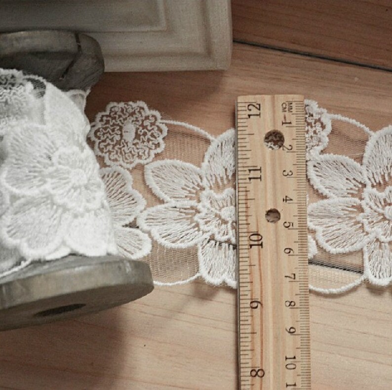 May include: White lace trim with a floral design, measured against a wooden ruler marked in inches.