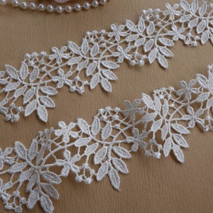 May include: White lace trim featuring a delicate floral design. The lace has a scalloped edge and is ideal for adding a touch of elegance to any project.