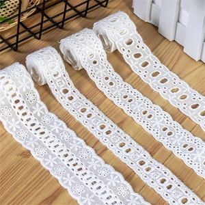 May include: Four rolls of white cotton lace trim with different patterns. The lace trim is delicate and intricate, with a variety of floral and geometric designs.