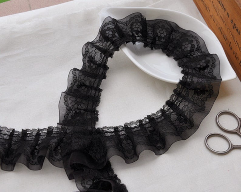May include: Black lace trim with a ruffled edge. The lace is delicate and has a floral pattern.
