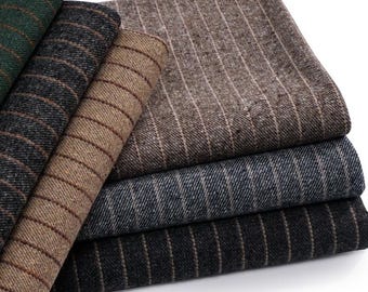 Puede incluir: Una pila de cinco muestras de tela dobladas con un patrón de rayas finas. Los colores incluyen verde oscuro, gris carbón, marrón claro, azul medio y negro. Cada pieza de tela tiene una apariencia tejida y texturizada con rayas verticales.