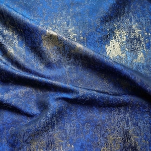 May include: A piece of fabric featuring a deep royal blue base color with a distressed, mottled texture. The surface is overlaid with metallic gold foil accents that create a scattered, weathered appearance across the folds of the material.