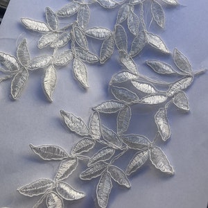 May include: White lace applique with a delicate floral design featuring leaves. The applique is perfect for adding a touch of elegance to any project.