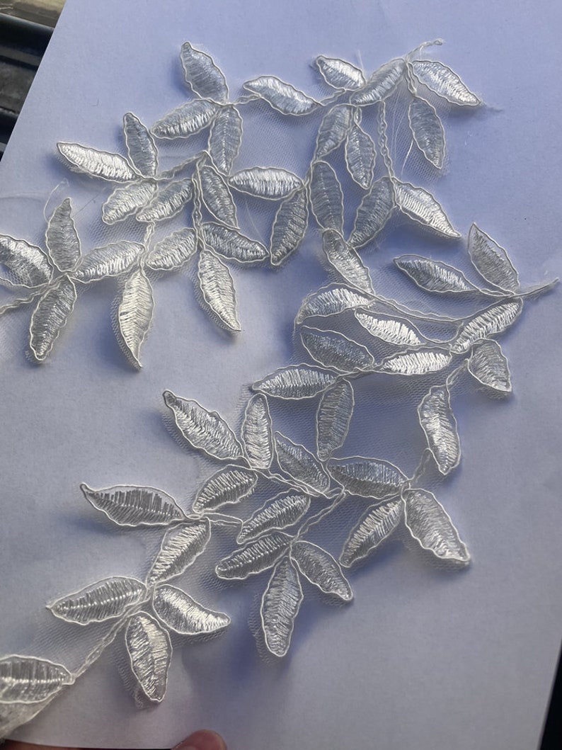 May include: White lace applique with a delicate floral design featuring leaves. The applique is perfect for adding a touch of elegance to any project.