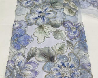 Könnte beinhalten: Ein transparenter, hellblauer Tüllstoff mit aufwendigen Blumenstickereien in Violett-, Blau- und Weißtönen. Die Blüten und Blätter sind mit silbernem Metallic-Garn, durchsichtigen Perlen und Pailletten verziert, was eine strukturierte Oberfläche ergibt.