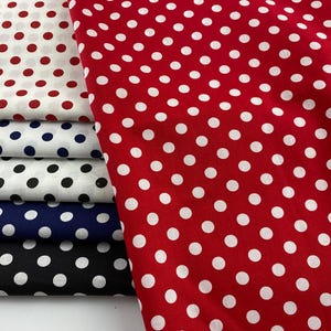 Può includere: Un mucchio di tessuto a pois in vari colori, tra cui rosso, bianco, nero e blu navy. Il tessuto presenta un motivo ripetuto di pois bianchi su uno sfondo colorato. Il tessuto è probabilmente cotone o un materiale simile.