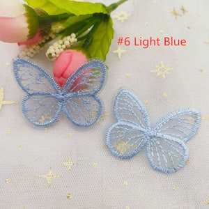 May include: Two light blue butterfly-shaped lace appliques on a white background with gold glitter stars. #6 Light Blue