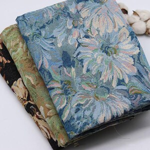 May include: Three folded pieces of woven fabric stacked together. The top layer features a blue and white floral pattern. The middle layer displays a green and brown botanical design. The bottom layer shows a black fabric with beige floral motifs.