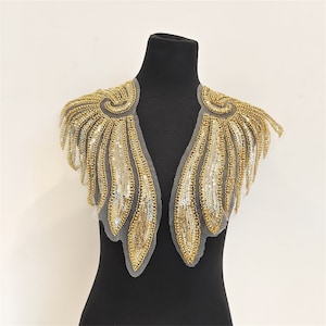 May include: Gold sequined fabric trim with a wing design. The trim is on a black mannequin and is perfect for adding a touch of sparkle to any garment.
