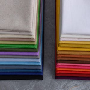 Peut inclure: Des piles d'échantillons de tissus de différentes couleurs, dont blanc, beige, vert, violet et bleu. Les échantillons sont soigneusement disposés, présentant une gamme de teintes et de textures. L'image met en évidence la variété des options de tissus disponibles.