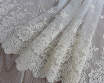May include: An off-white lace fabric featuring a scalloped edge and intricate floral embroidery. The sheer mesh base is decorated with repeating patterns of flowers, leaves, and vines, creating a delicate texture across the entire length of the material.