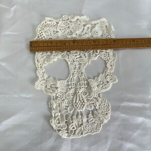 May include: White lace skull applique measuring approximately 7 inches wide. The skull is detailed with intricate floral designs.