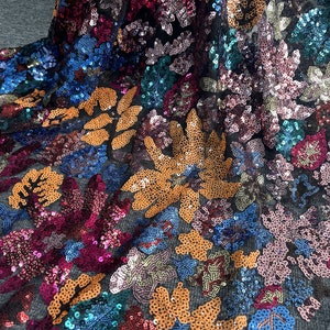 Puede incluir: Una tela de malla negra con lentejuelas de colores en forma de flores. Las lentejuelas son en tonos de naranja, rosa, azul y verde.