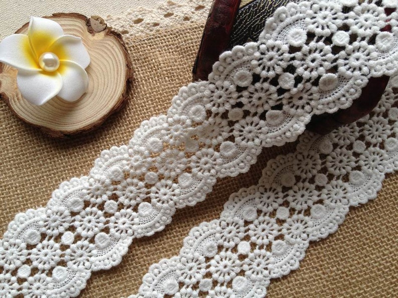 May include: White cotton lace trim with a delicate floral pattern. The lace has a scalloped edge and is perfect for adding a touch of elegance to any project.