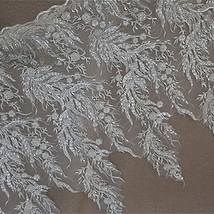 May include: White lace fabric with a silver glitter pattern of floral sprigs and leaves.
