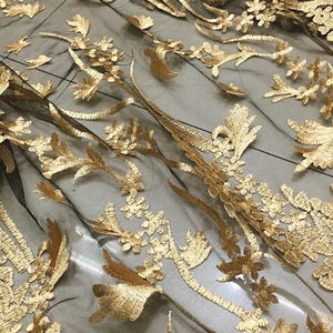 May include: Black mesh fabric with gold embroidered floral designs. The fabric has a delicate and intricate pattern.