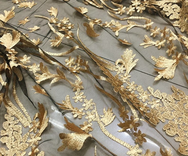 May include: Black mesh fabric with gold embroidered floral designs. The fabric has a delicate and intricate pattern.