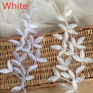 May include: Two white lace appliques in the shape of leafy branches. The appliques are on a woven wicker surface. The text "White" and "Ivory" is visible above the appliques.
