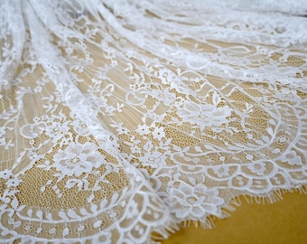 May include: White lace fabric with a delicate floral pattern. The lace is soft and sheer, with a slightly textured surface.