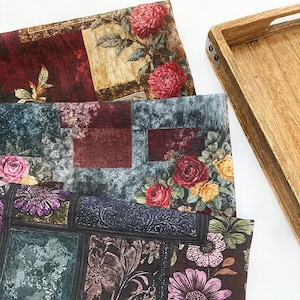 May include: Three floral patterned fabrics with a wooden tray. The fabrics feature a variety of flowers, including roses and dahlias, in shades of red, pink, and purple. The tray is made of light brown wood with metal accents.