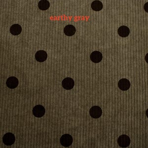 May include: A textured corduroy fabric in an earthy gray tone featuring a repeating pattern of solid dark brown polka dots. The surface displays vertical ribbed lines characteristic of corduroy material, with the text earthy gray visible.