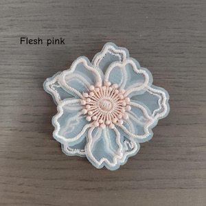 May include: A flesh pink embroidered flower applique featuring a sheer, translucent base with delicate, light pink thread detailing along the petals and a textured, circular center. The text "Flesh pink" is printed in the upper left corner.