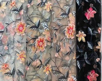 May include: Close-up of three fabric samples with floral embroidery. The fabrics are in shades of ivory, tan, and black. The embroidery features orange, pink, and yellow flowers with dark gray leaves and stems. The sheer fabric is suitable for apparel and craft projects.