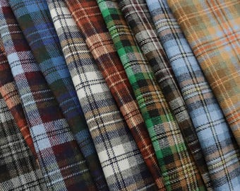 Può includere: Una collezione di campioni di tessuto a quadri in vari colori, tra cui blu, marrone, verde e beige. Il tessuto presenta un classico motivo a scacchi, con ogni campione piegato e stratificato per mostrare le diverse combinazioni di colori e trame.