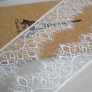 May include: White lace trim with a delicate floral pattern. The lace has a scalloped edge and a frayed finish.