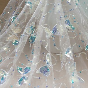 May include: White tulle fabric with iridescent sequins and blue butterfly designs.